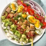 A colorful Cobb Salad with grilled chicken, bacon, avocado, tomatoes, and hard-boiled eggs, topped with a tangy vinaigrette dressing.