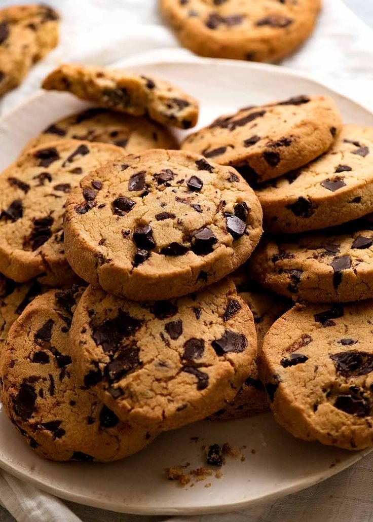 A close-up of freshly baked chocolate cookies stacked on a wooden tray with melting chocolate chips.