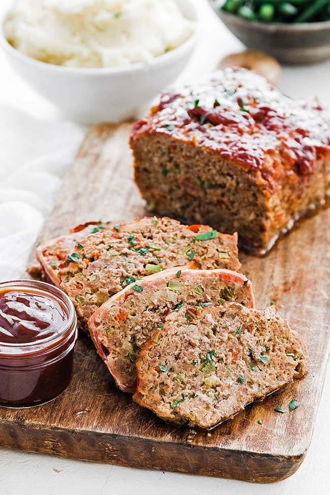  A perfectly baked meatloaf on a serving platter, glazed with a sweet and savory tomato sauce, garnished with fresh herbs, and sliced for serving.